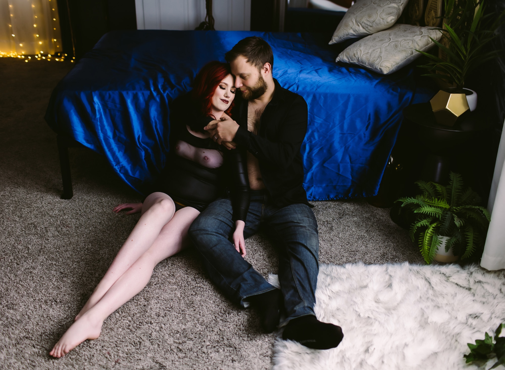 couple sitting on floor in front of bed snuggling