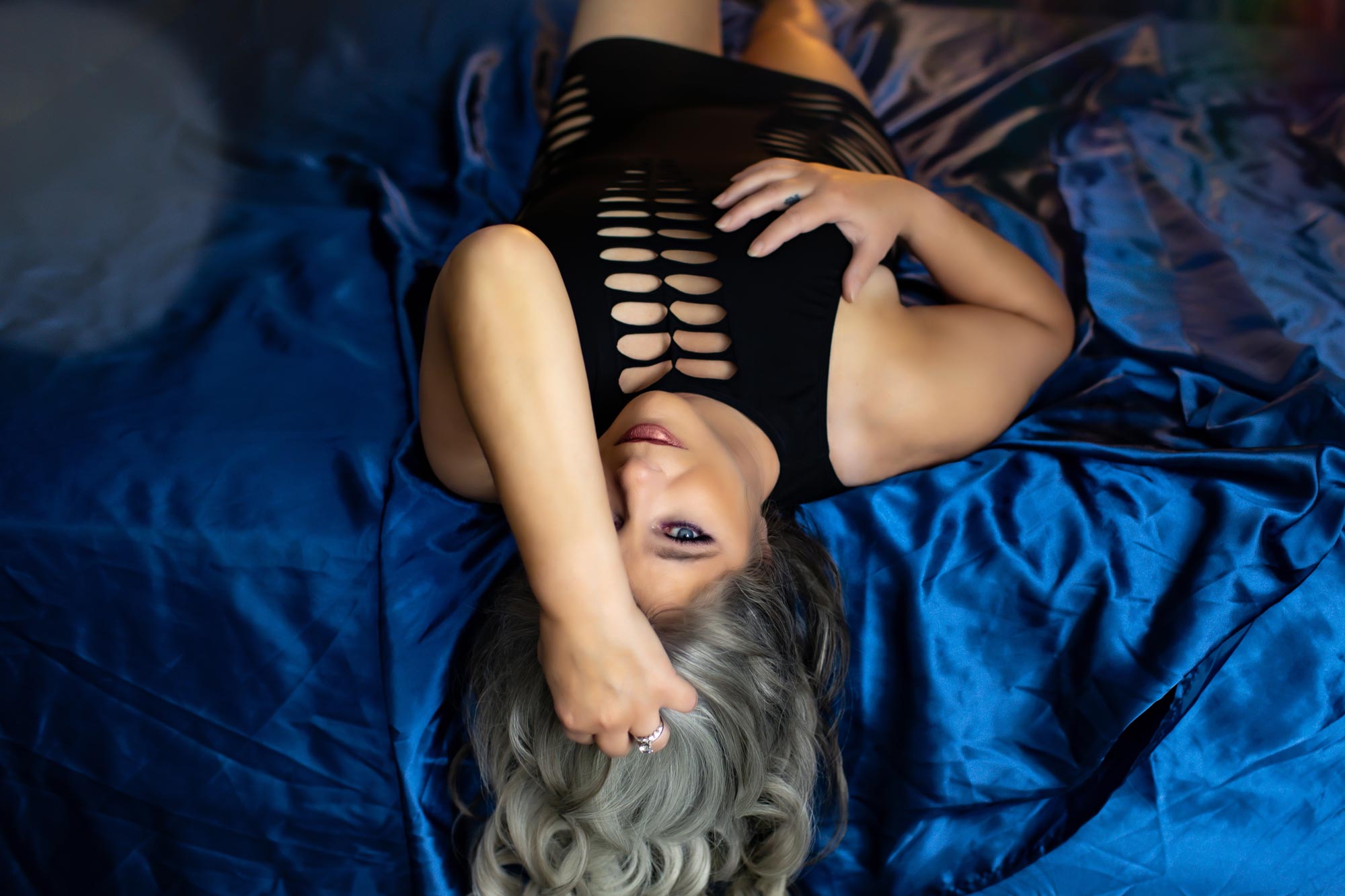 grey haired beauty laying on blue sheets with hand in her hair