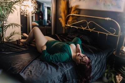 woman in emerald green bodysuit laying on black satin sheets