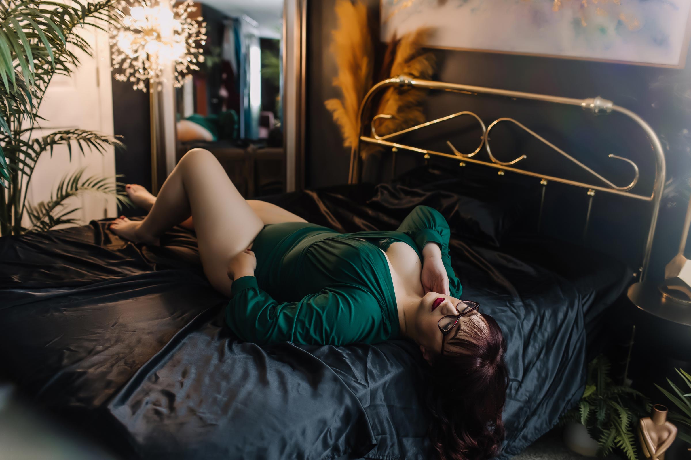 woman in emerald green bodysuit laying on black satin sheets